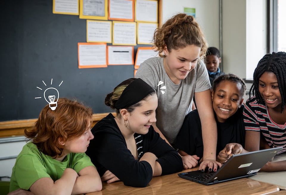 Group of smiling students gathered together around a desk and looking at an unidentified object in front of them