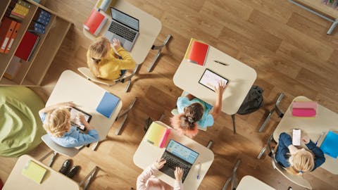 Three smiling students sitting in a classroom looking at a computer tablet with the Classcraft platform
