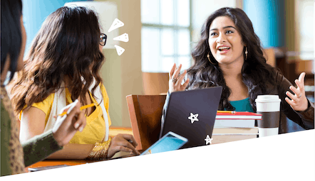 Two women in a conversation at a table with their computers