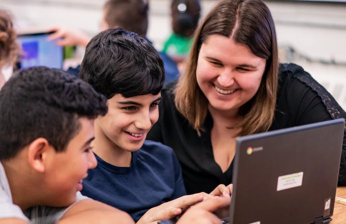 Teacher with two students looking to a chromebook at their desk
