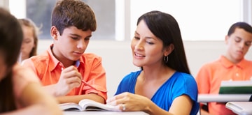 Alumno en su escritorio haciendo una pregunta a su profesor