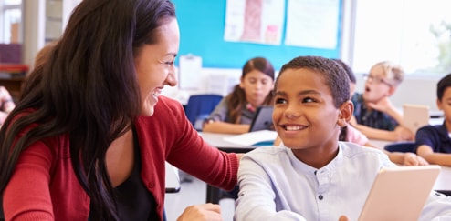 Alumno con una tableta en las manos con su profesor sonriendo mientras le explica algo