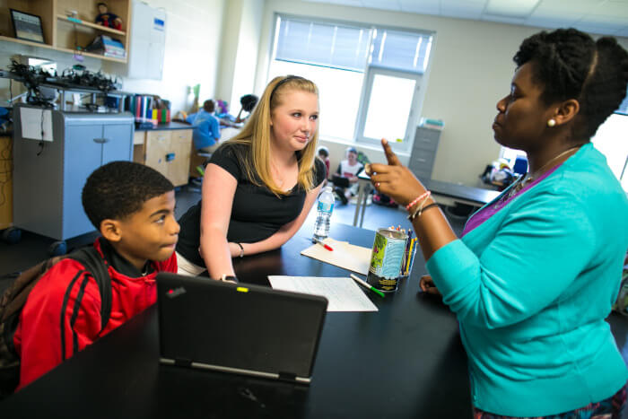 teacher explaining something to two students with her hand raised