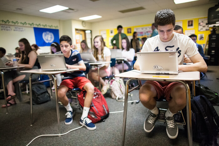 Students in class seated at their individual desks working on an assignment on their laptops